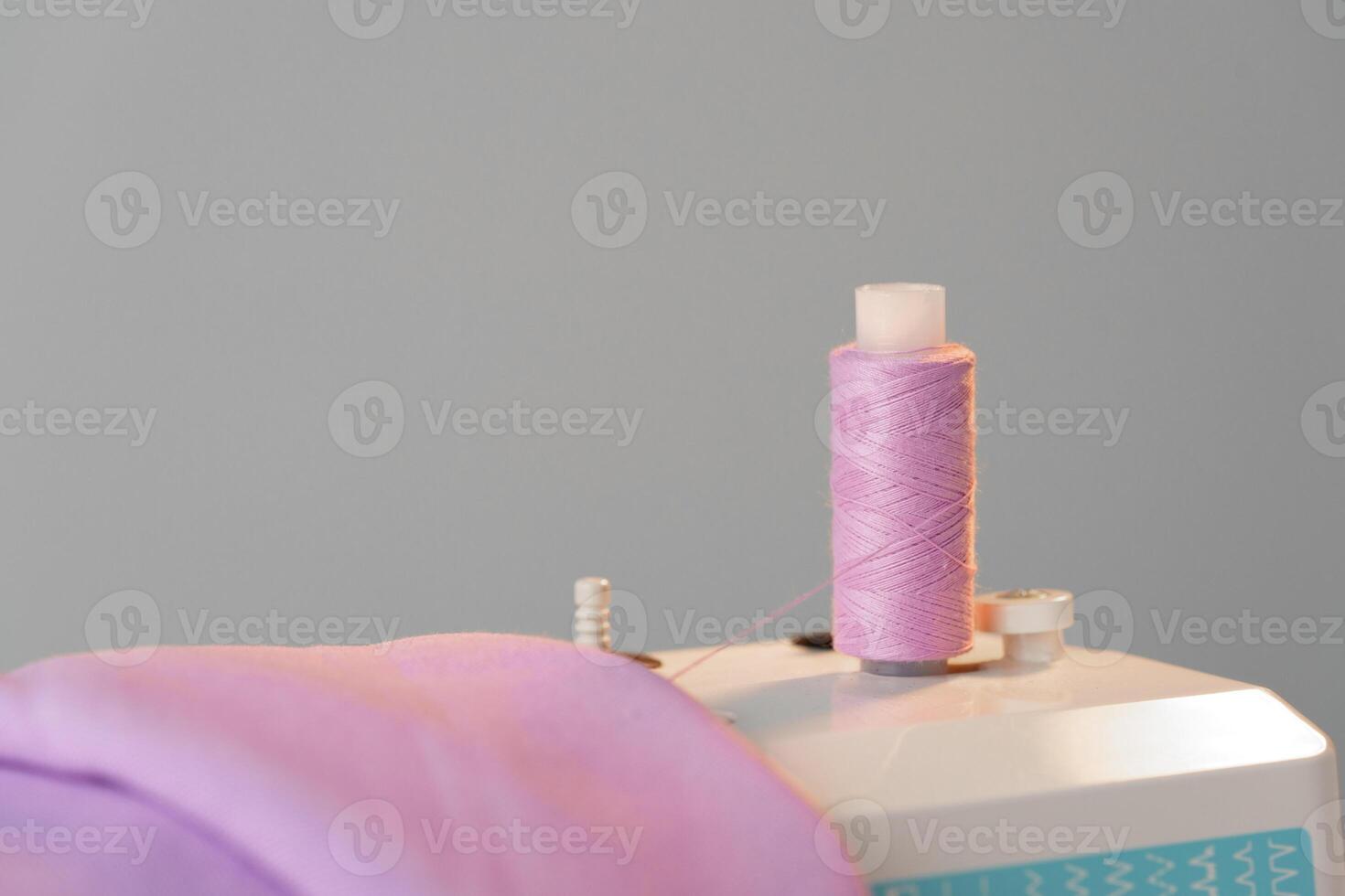 View of a sewing machine with a spool of pink thread placed on top photo