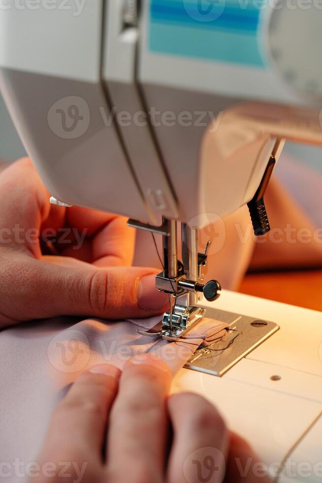 Hands sewing fabric using a sewing machine on a wooden table in a well-lit workspace photo