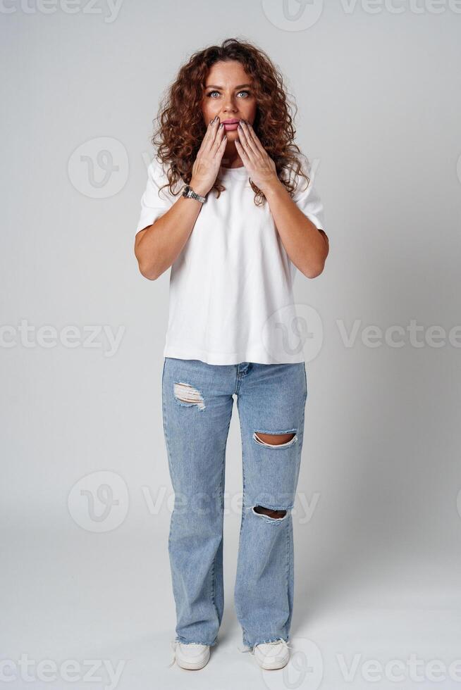 Surprised woman expressing strong emotions with wide eyes and raised hands, studio setting photo