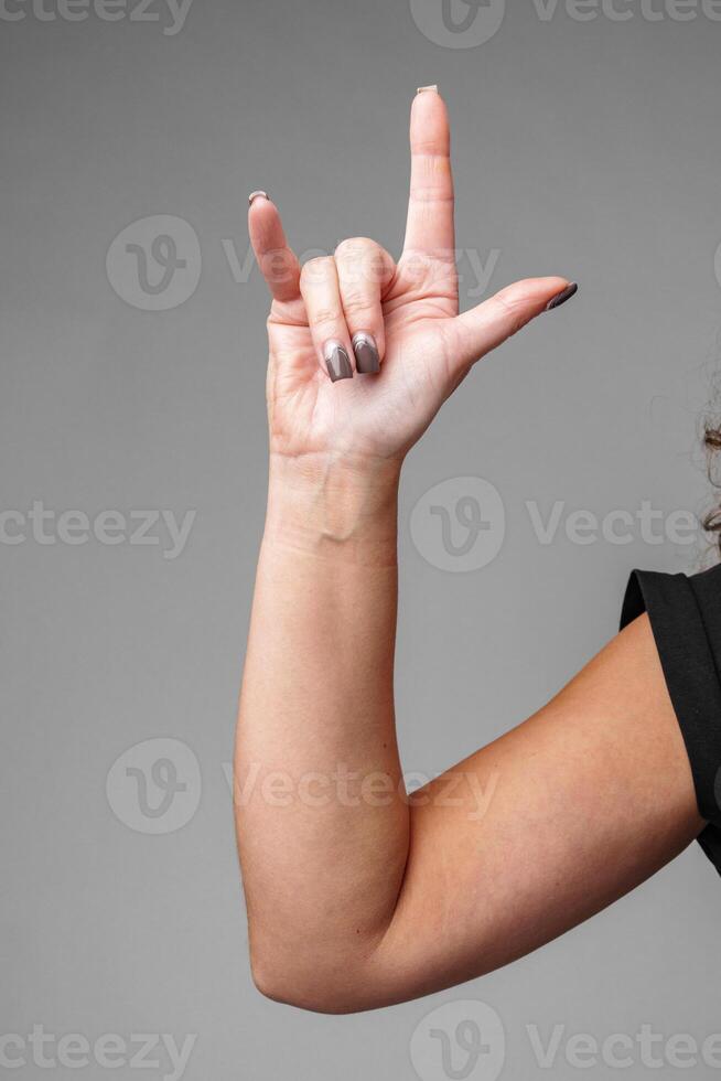 A person making the I love you gesture with their hand in front of a neutral gray background photo