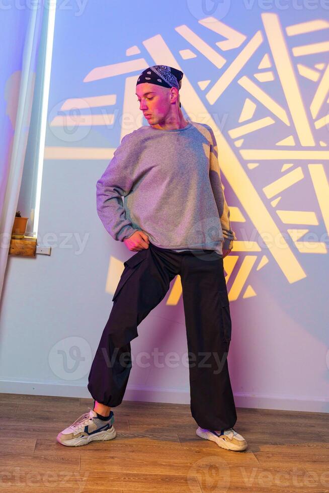 A young man wearing a bandana and a grey sweatshirt strikes a pose in a dance studio with a colorful backdrop photo