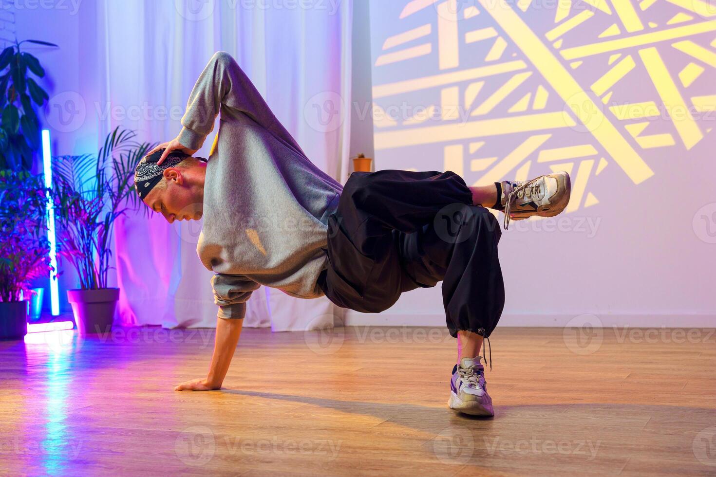 A young man practices a breakdancing move in a studio with colorful lighting photo