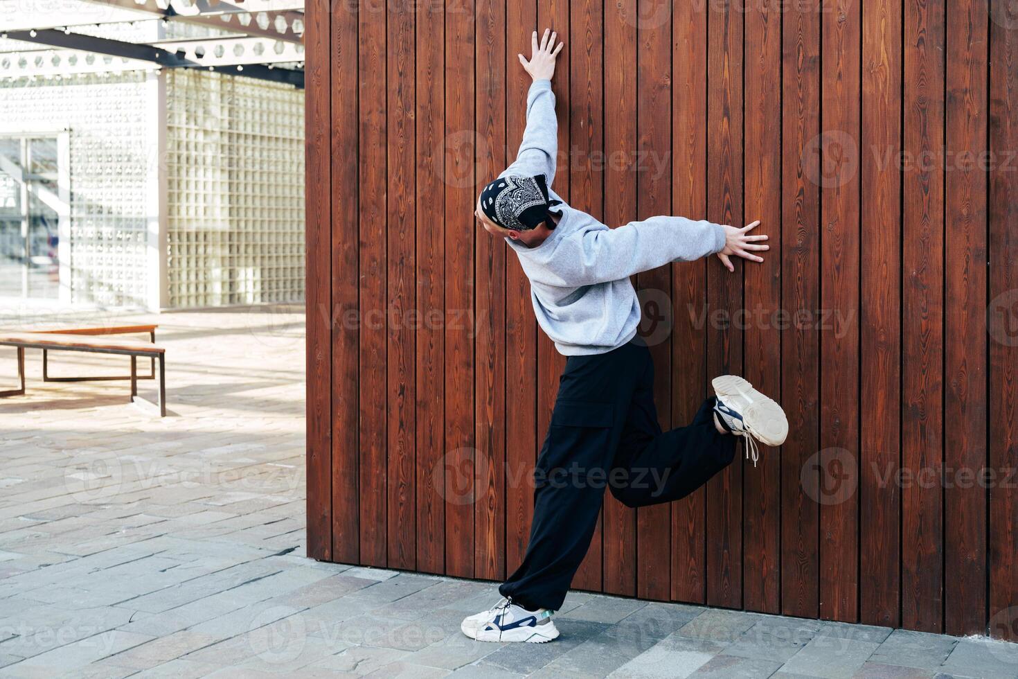 A young man in a grey sweatshirt and black pants is practicing parkour against a wooden wall photo