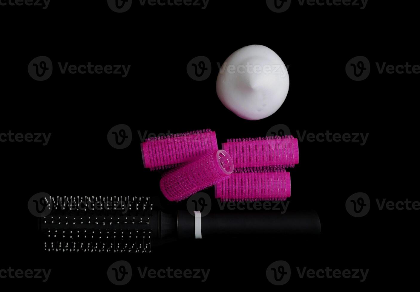 Different products for hair styling - comb, curlers and volume styling mousse isolated on black background with copy space photo