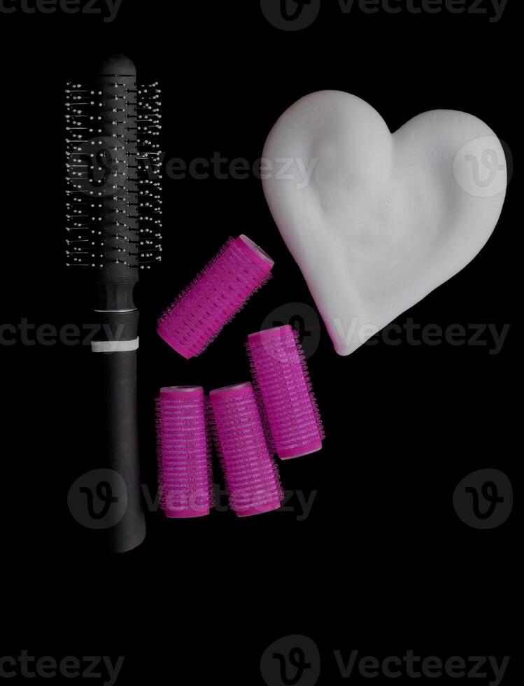 Different products for hair styling - comb, curlers and volume styling mousse isolated on black background with copy space photo