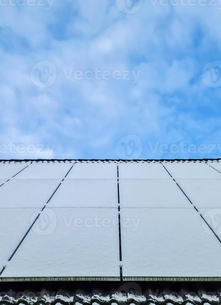 Snow covered solar panels producing clean energy on a roof of a residential house. photo