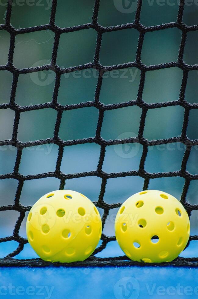 two pickleball balls on a blue pickleball court, with the net in the background photo