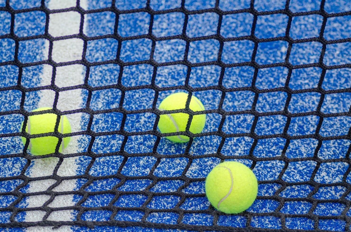 three paddle tennis balls behind the net of a paddle tennis court, background for racket sports concept photo