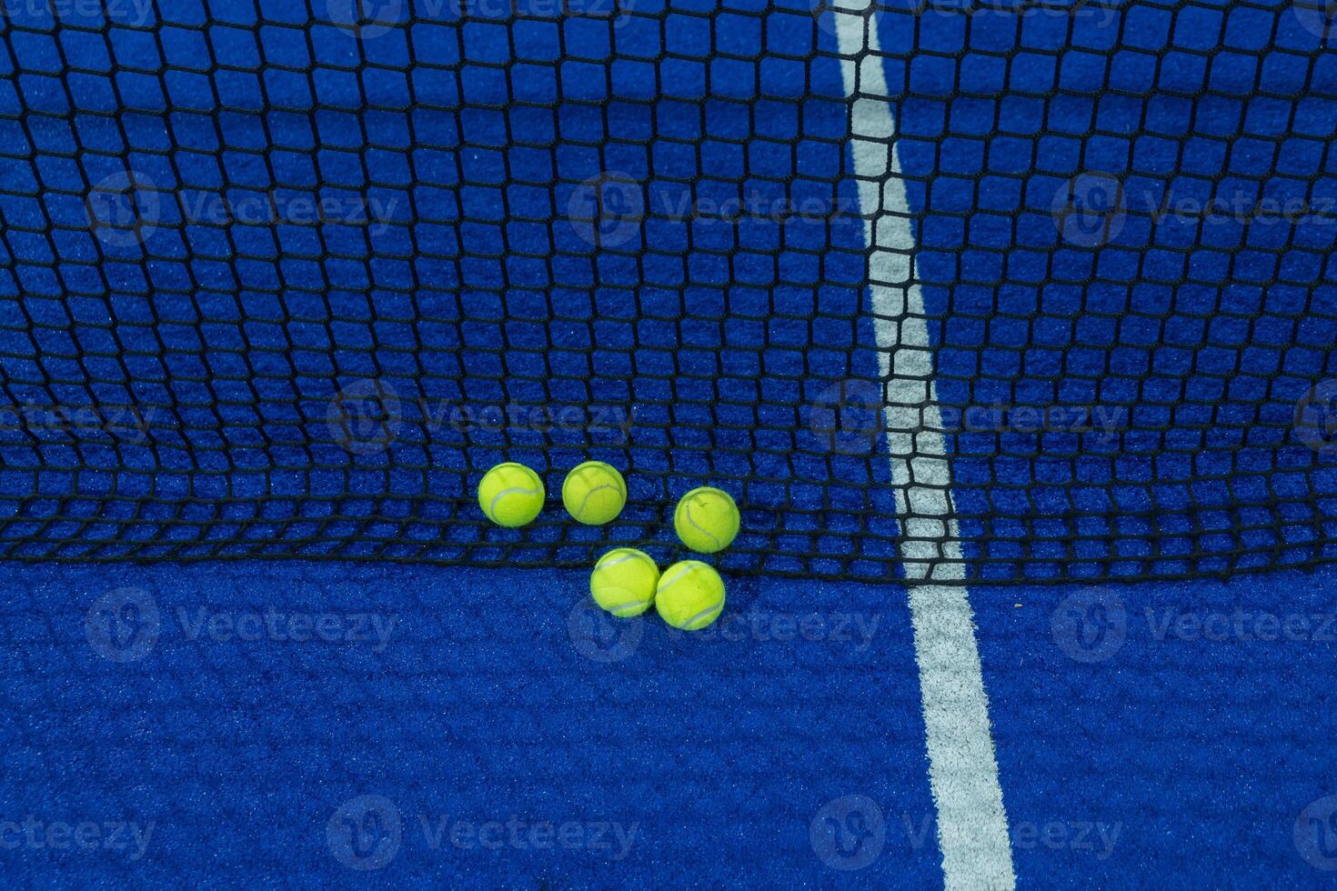 Multiple balls in the net of a blue paddle tennis court. photo