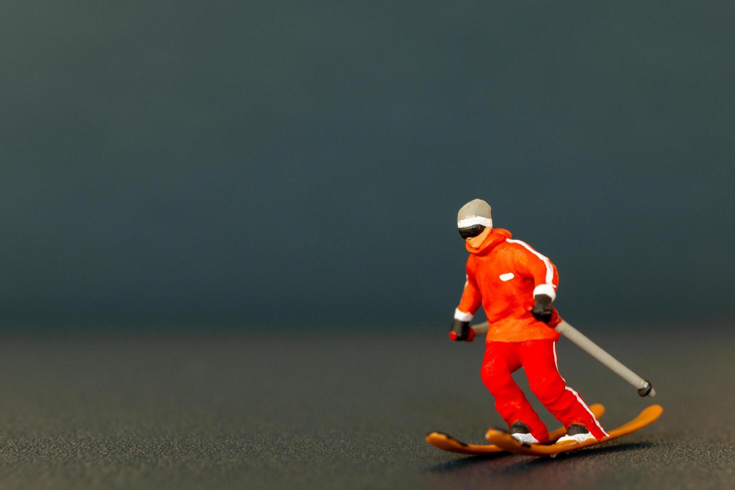 Miniature figurine of a skier is detailed with vibrant colors, set against a dark blurred background photo