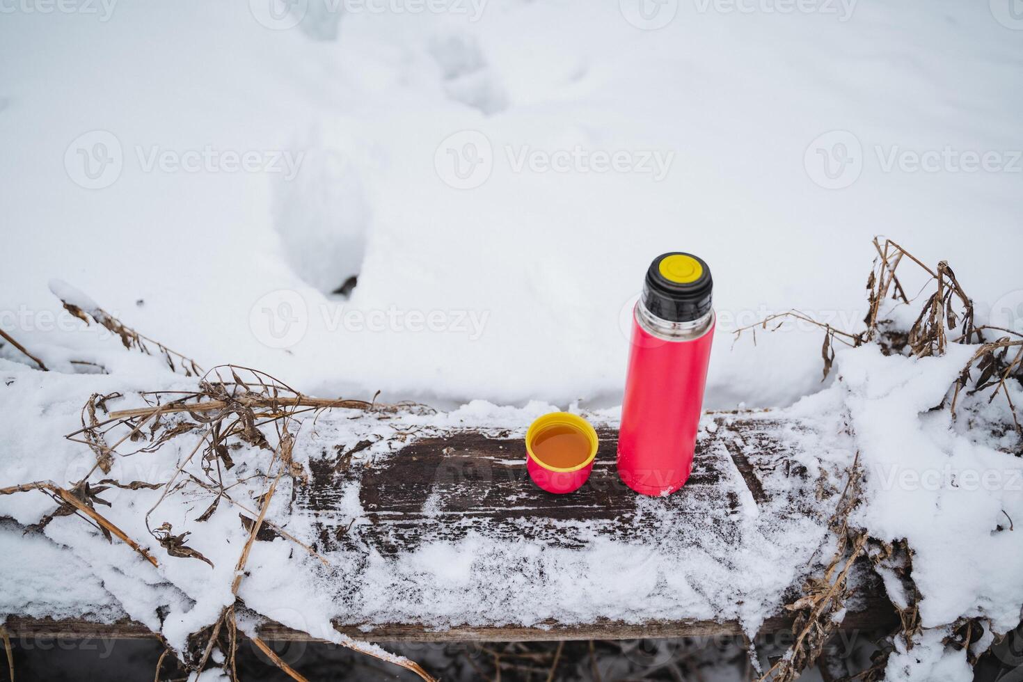 A thermos with a mug stands on a wooden table in the forest in winter, pink tourist utensils, thermo flask. photo