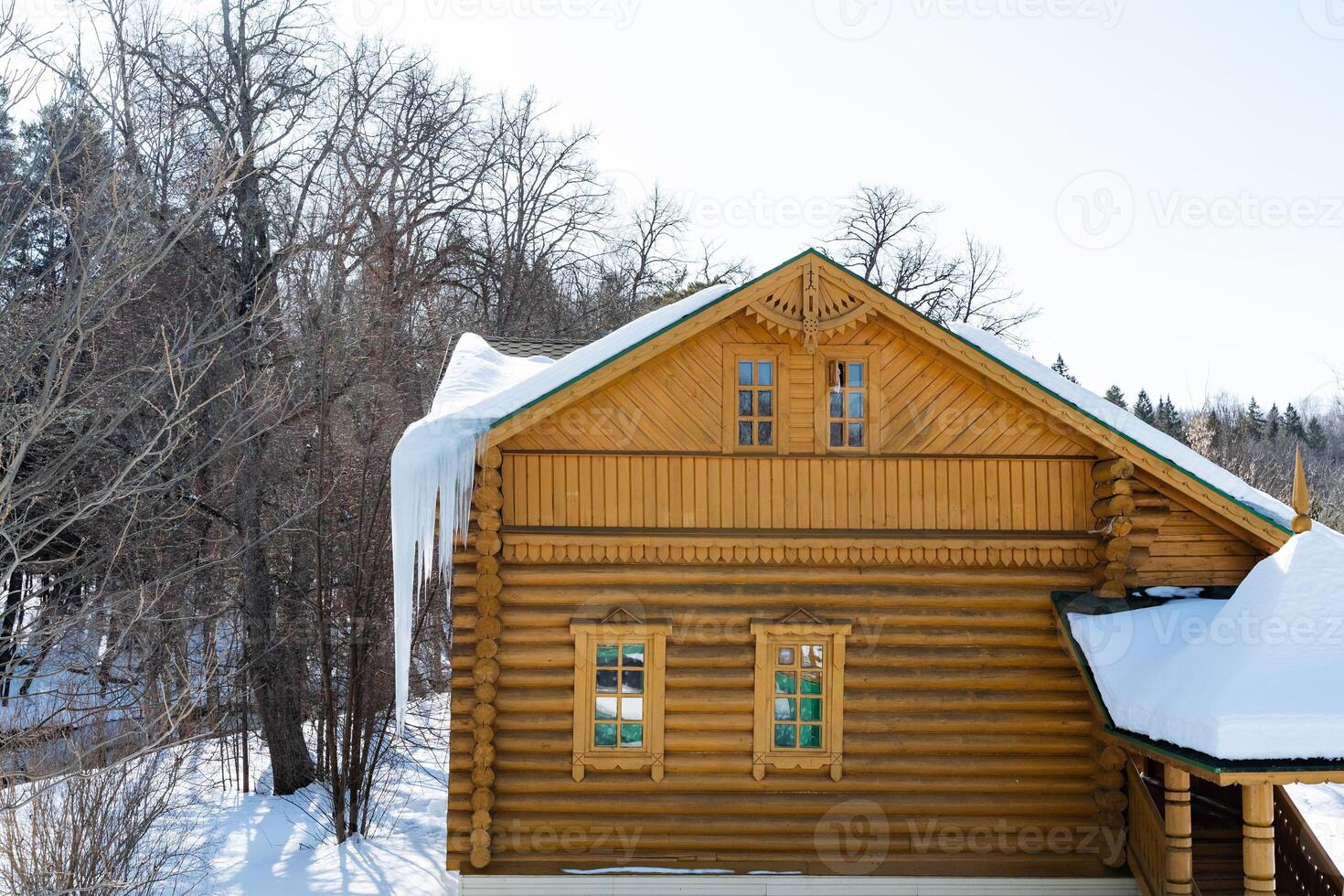 Snowcovered log cabin with icicles on the roof, overlooking a forested slope photo