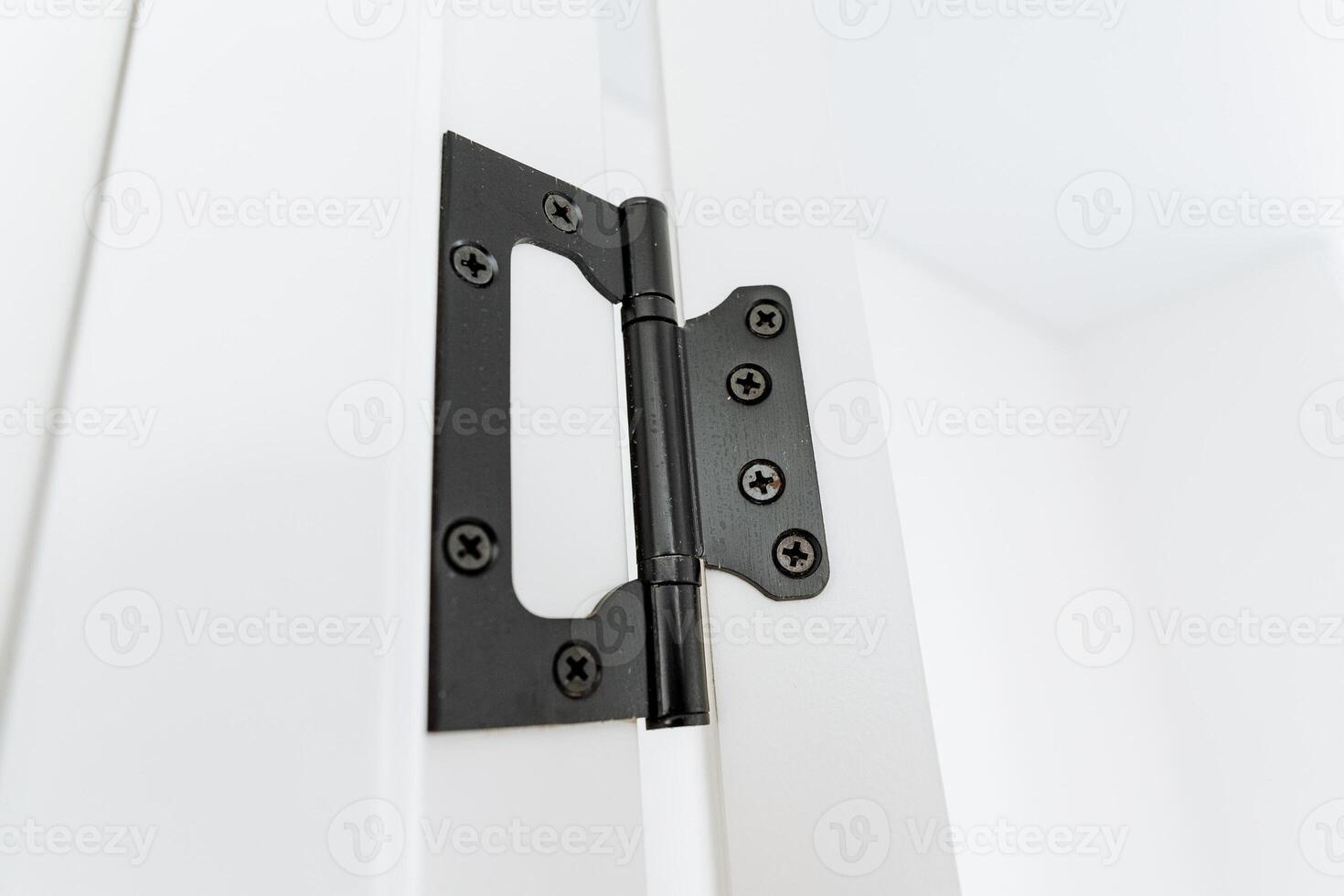 Metal black door hinge on white rectangle wood door. Household hardware detail photo