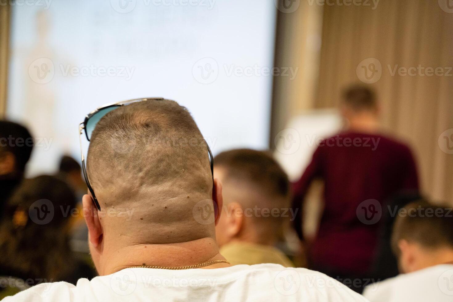A man in sunglasses sits in a classroom watching a presentation photo