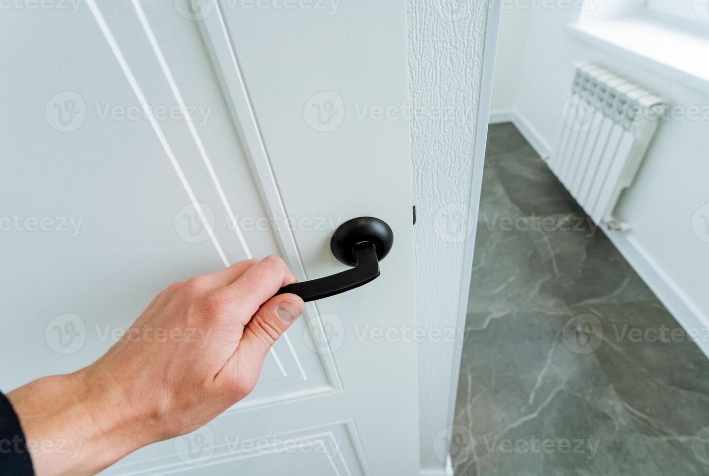 With a swift gesture, the person opens the white door with a black handle photo