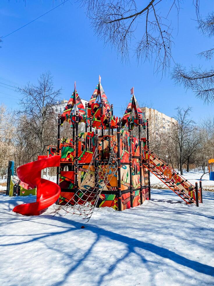 A vibrant snowy playground with a red slide on a city slope photo
