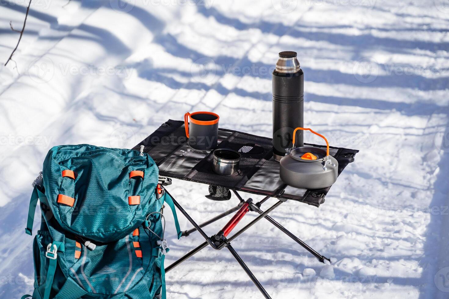 Hiking equipment for hiking stands on the snow in winter in the forest, folding table made of mesh and aluminum legs. Tableware for food photo