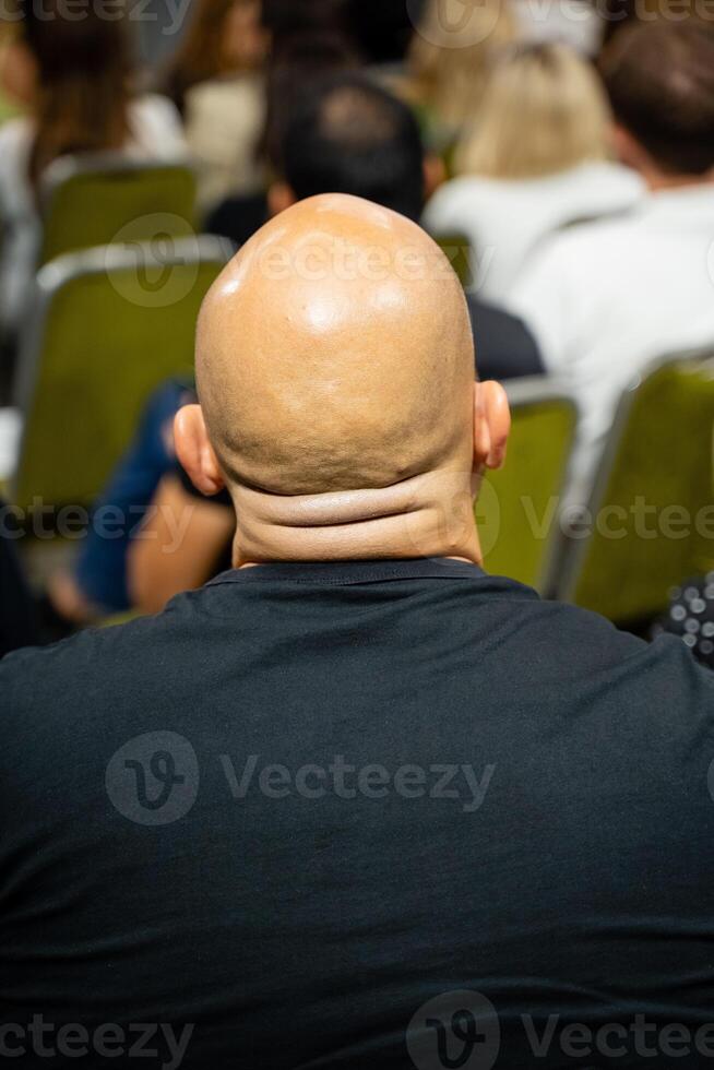 A bald man leads a conference, engaging an attentive audience and passionately promoting collaboration and learning among participants photo