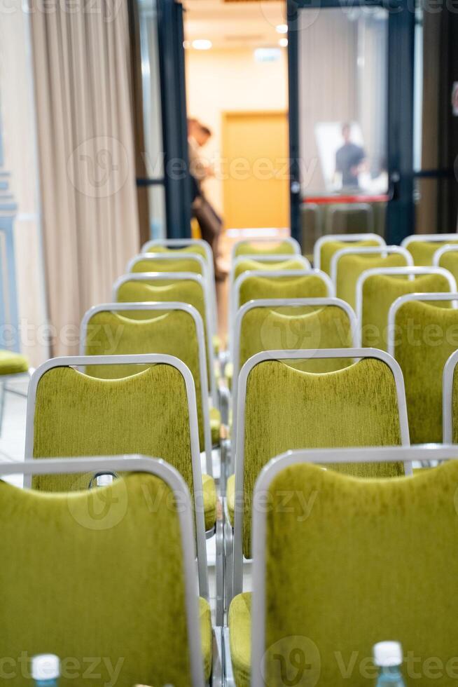 A conference room has rows of green chairs with water bottles photo