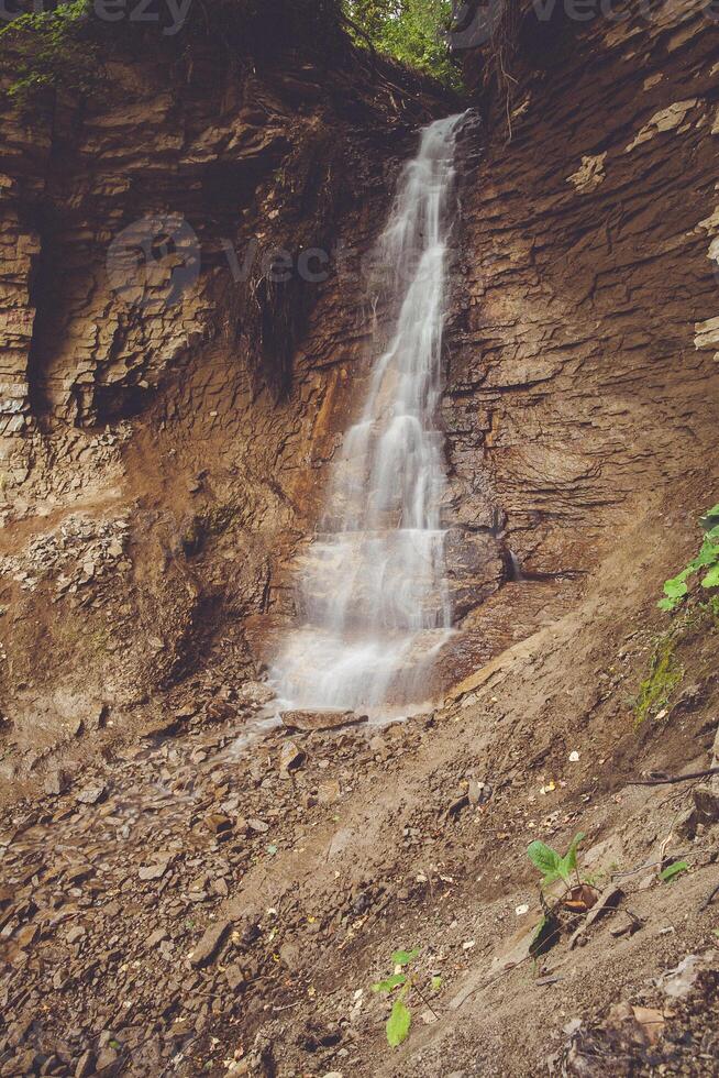 A beautiful waterfall cascades over a rocky cliff in a lush forest setting photo