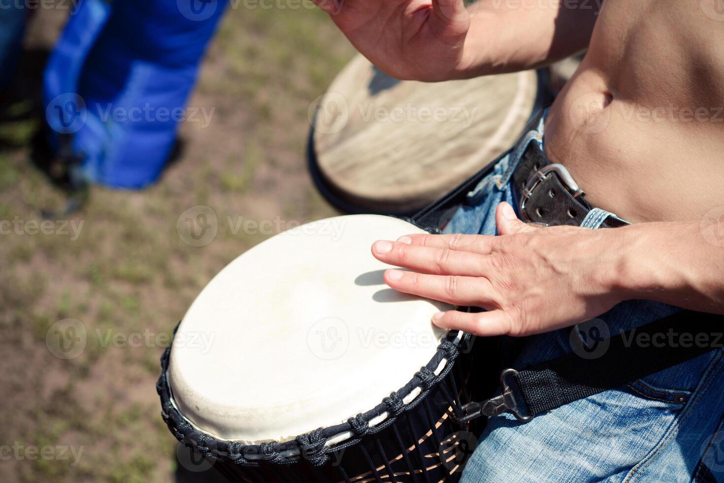 Man playing a djembe drum without a shirt outdoors on grass photo