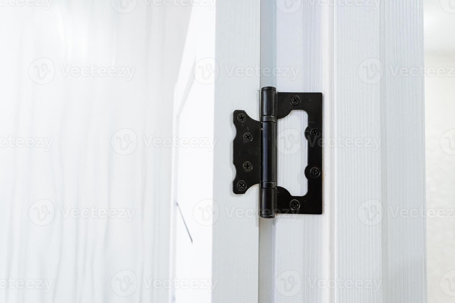 A closeup view displaying a black door hinge affixed on a white door photo