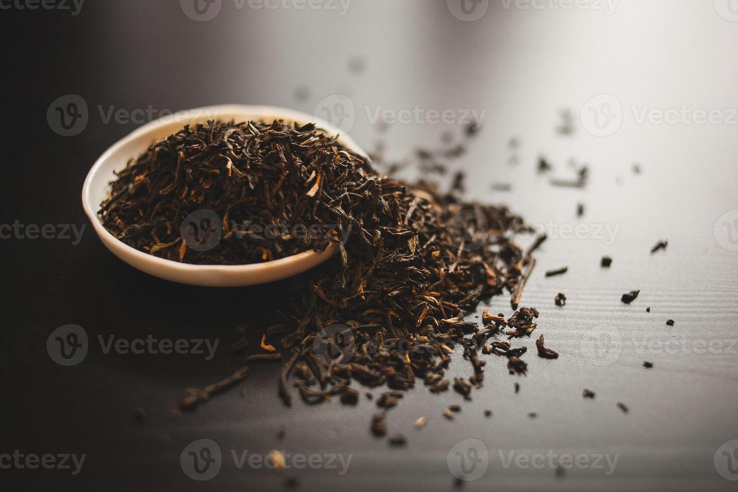 Liquid tea in a bowl sits beside a stack of tea leaves on a table photo