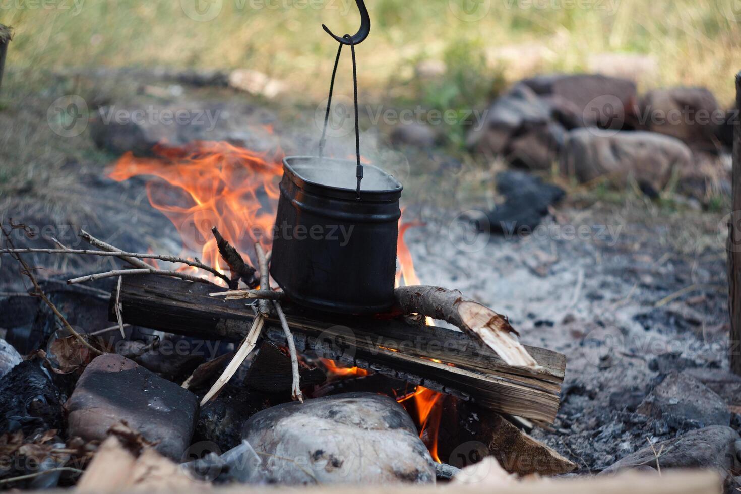 A pot of water boils over a fire in a natural landscape photo