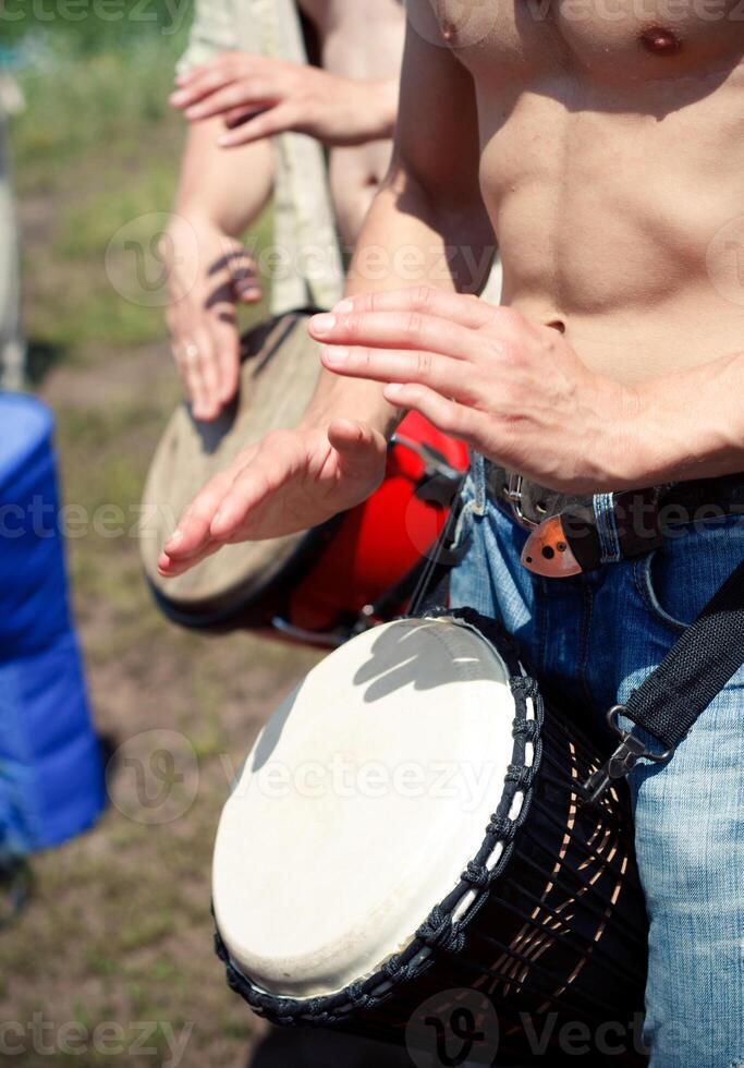 Shirtless vertebrate playing a djembe in a field, enjoying leisure and fun photo