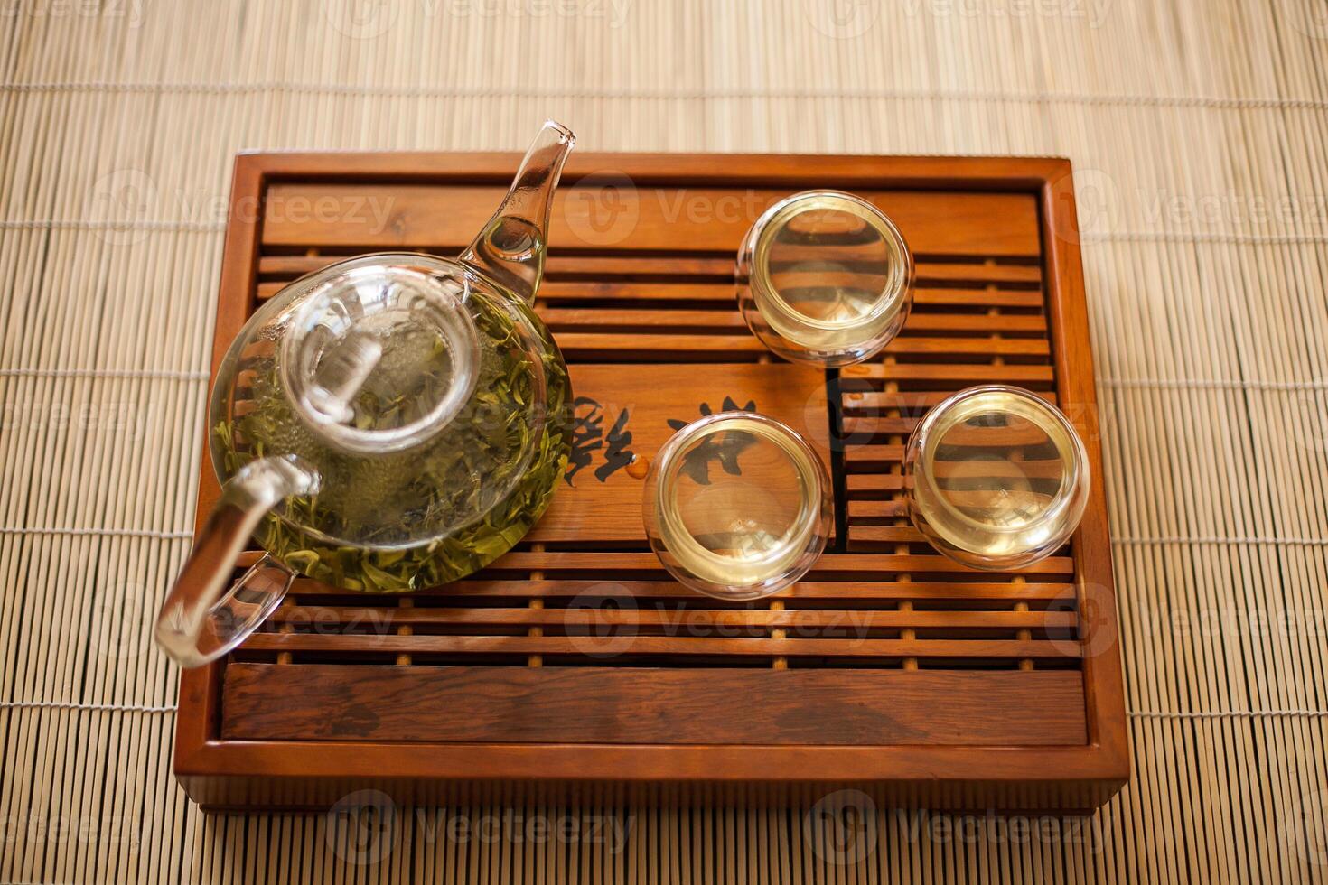 An antique glass teapot and three tea cups displayed on a wooden tray photo