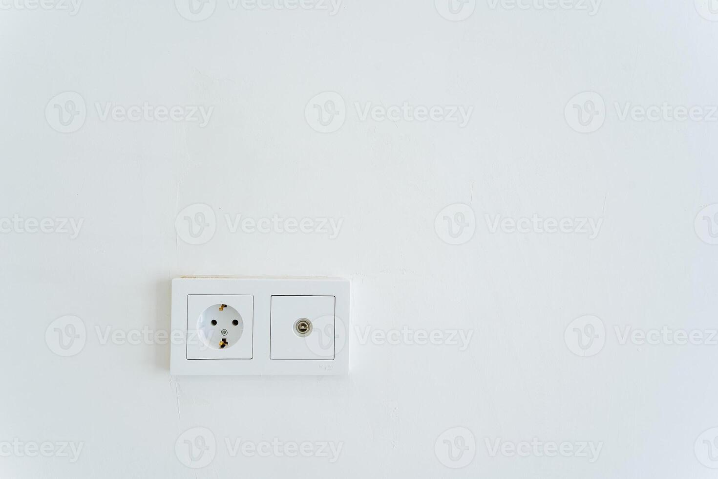 A rectangular white wall socket with a power plug and socket for electrical supply. photo