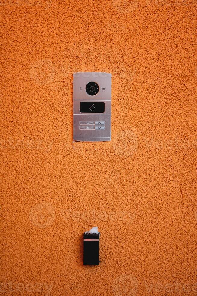 Modern door intercom system with camera isolated on orange wall background photo