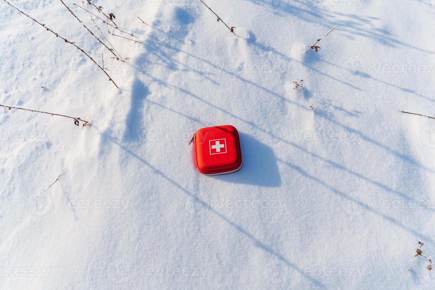 On the snow there is a first-aid kit, a conceptual photo of medical aid on a hike, a red box with medicines.