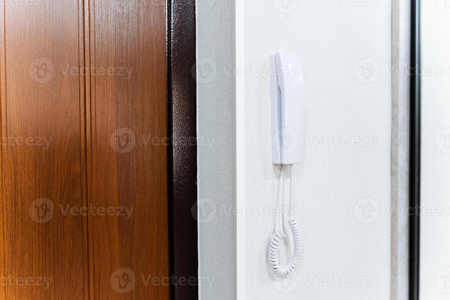 A white intercom hangs on the wall near the front door of the house. Telephone handset with wire, call the hotel administrator by phone. photo