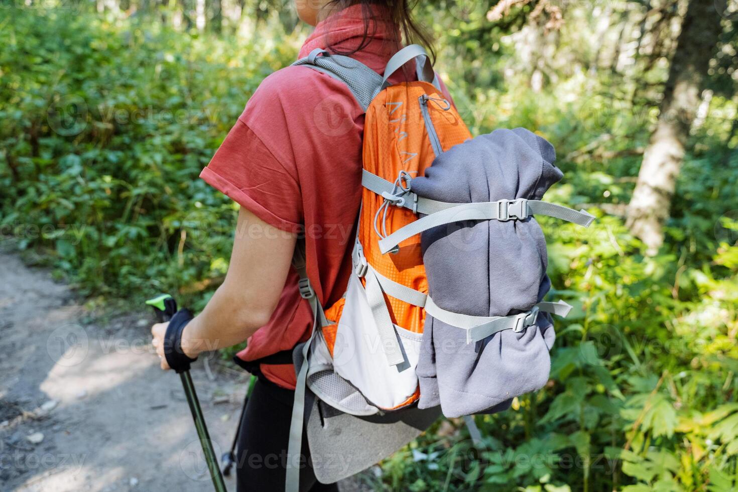 View from the back of a tourist backpack with things, equipment for hiking, straps on a backpack, a girl walking in the forest with poles, trekking. photo