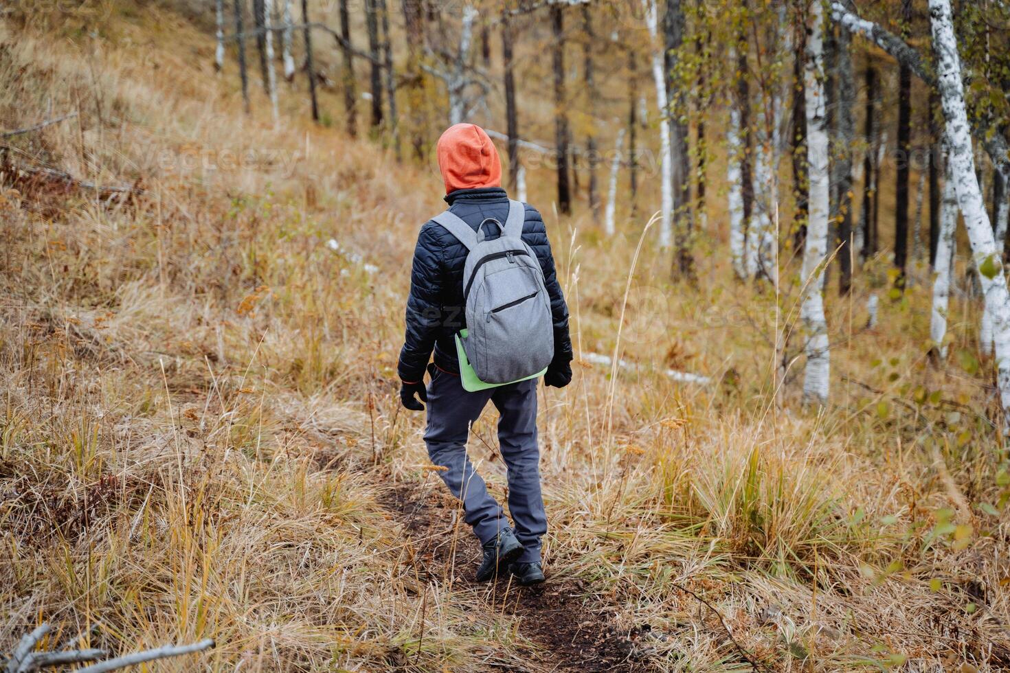 A man with a backpack on his back confidently walks along a mountain trail, a hiker on a hike moves along the azimuth, autumn hiking in a national park. photo