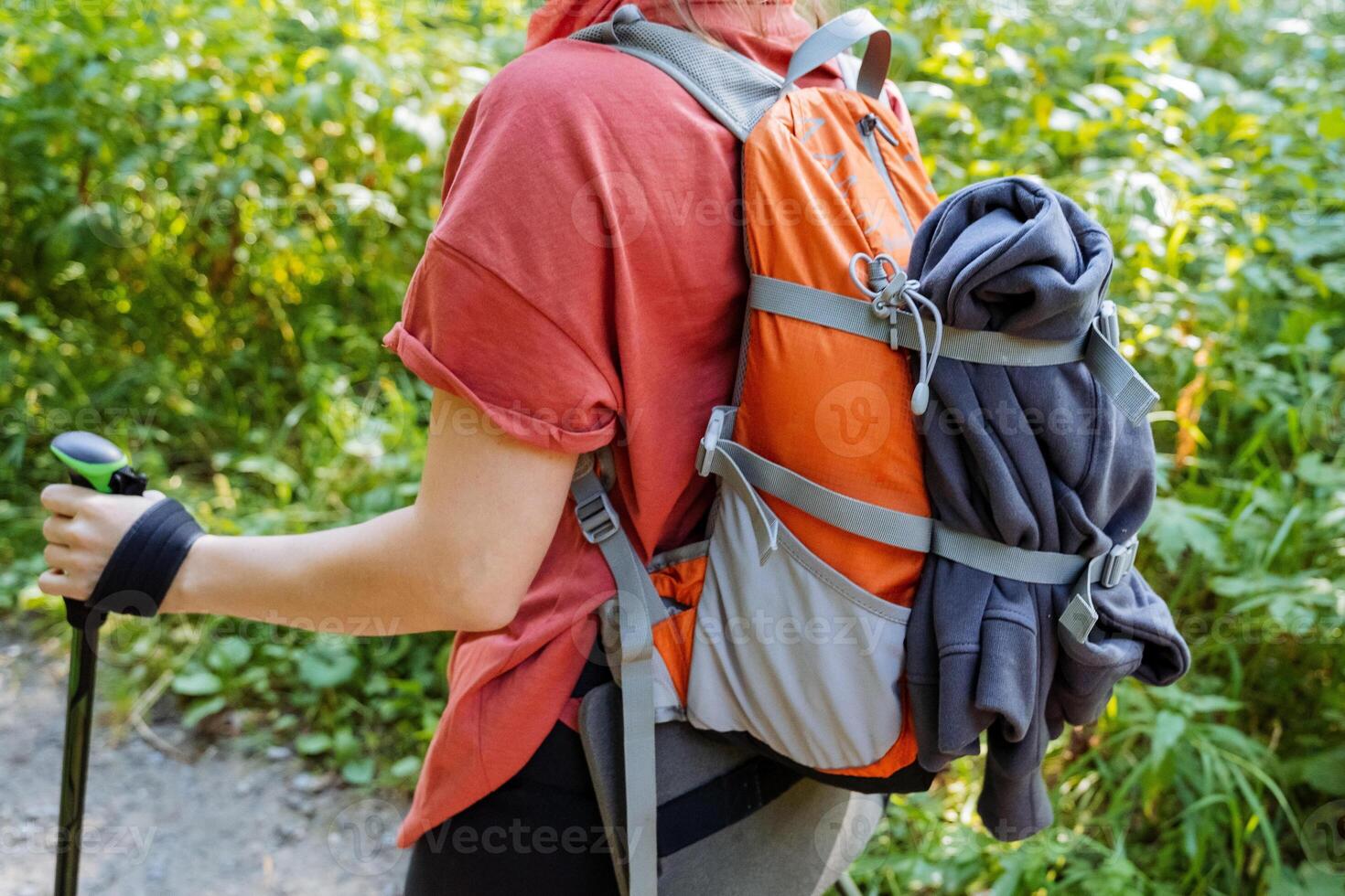 Man with backpack for things on a hike, girl tourist walking in the mountains, trekking with a backpack, a jacket fastened to a bag, a hand with a trekking pole. photo