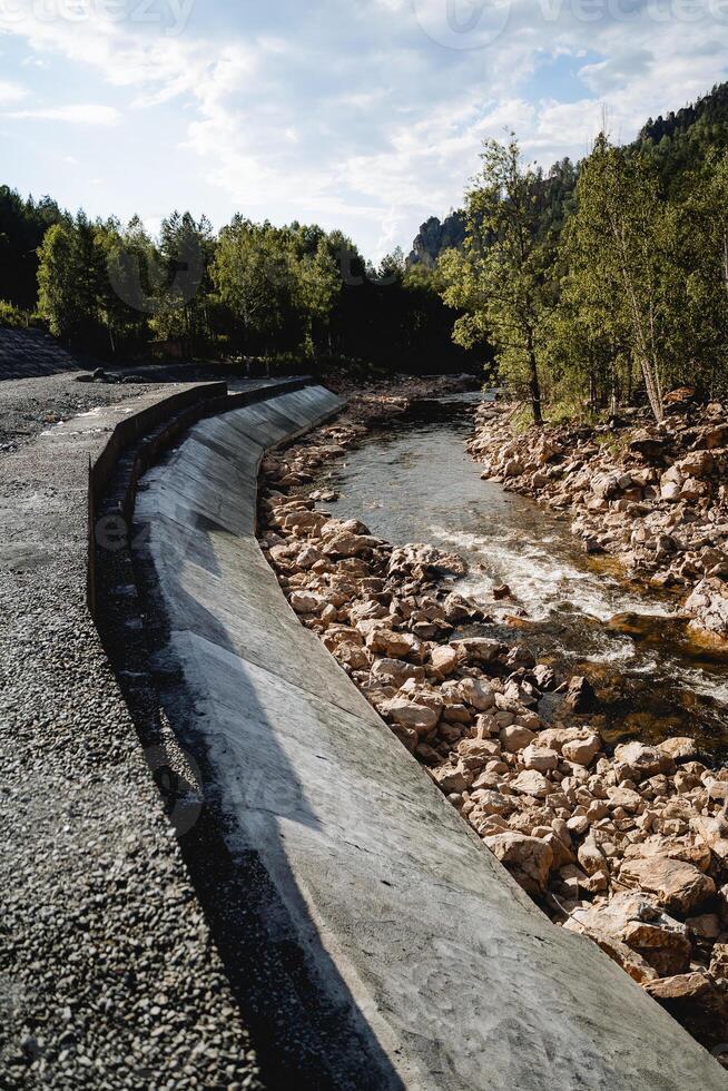 The dam is protective, concrete screed of the river coastline, protection of the roadway from flooding, mountain river, human intervention in nature. photo