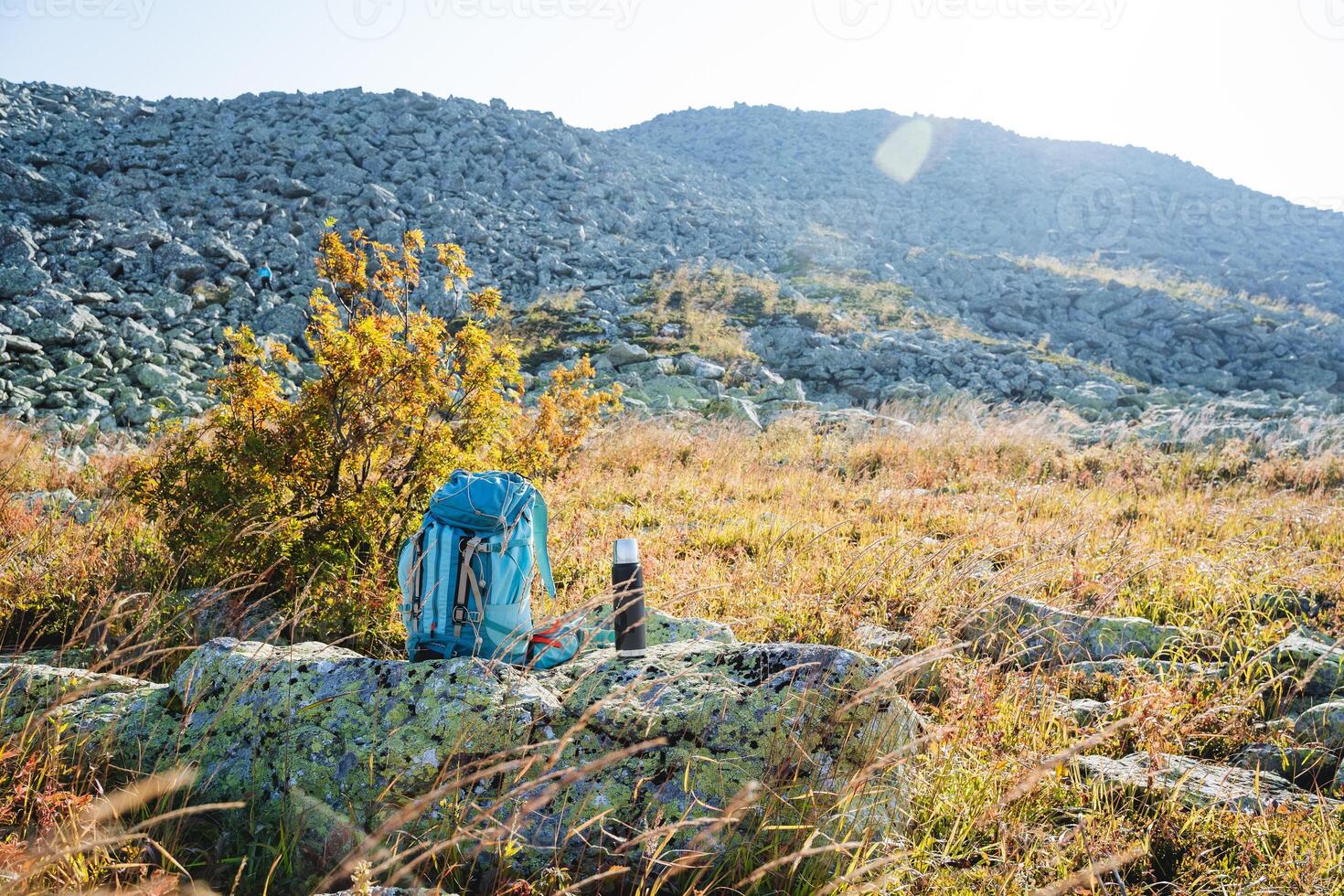 tourist equipment, a backpack for a hike stands on a stone, mountain tourism, a thermos with tea stands on a stone, a sunny day, autumn in the mountains. photo