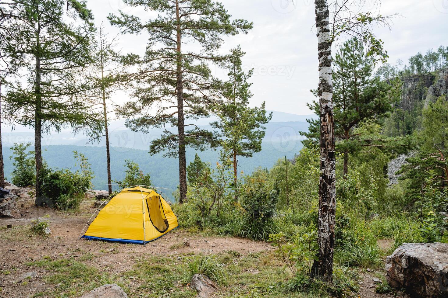 A yellow tent stands on the edge of a cliff in the mountains, a house for sleeping in nature, camping in the forest, a camp site, a tourist parking lot. photo