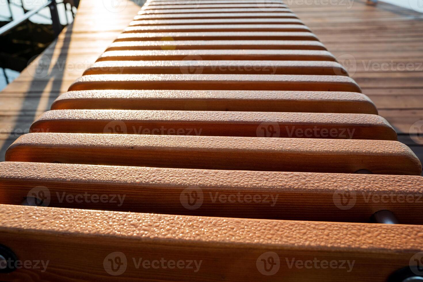 Drops of ross on the boards shine in the rays of the morning sun, a pattern of wood, a wet park bench, a wooden product. photo