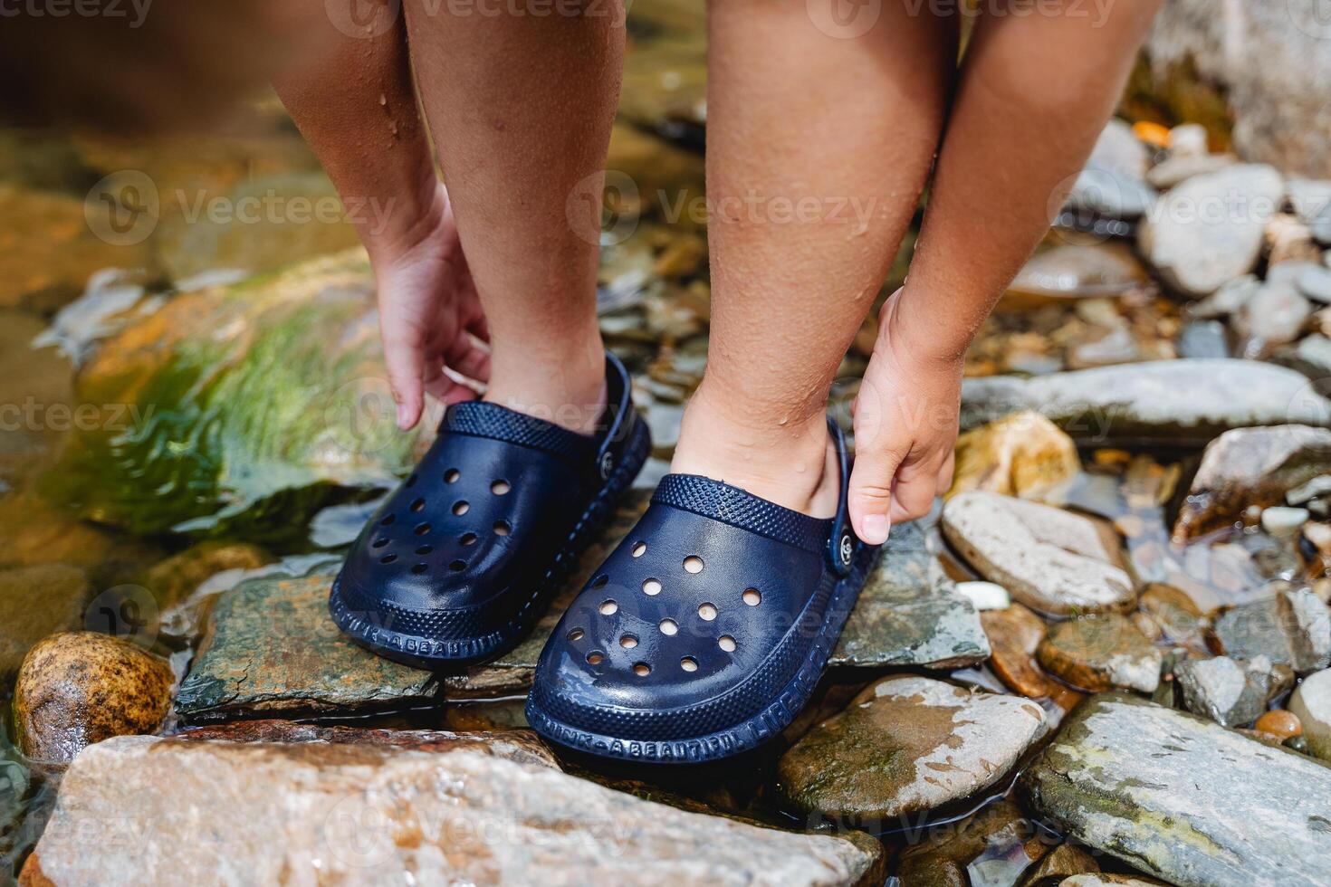 The child's feet are shod in slate, the boy wears shoes for swimming in the sea, protection of the feet from cuts, slaps for swimming, the boy stands on the bank of a stone river photo
