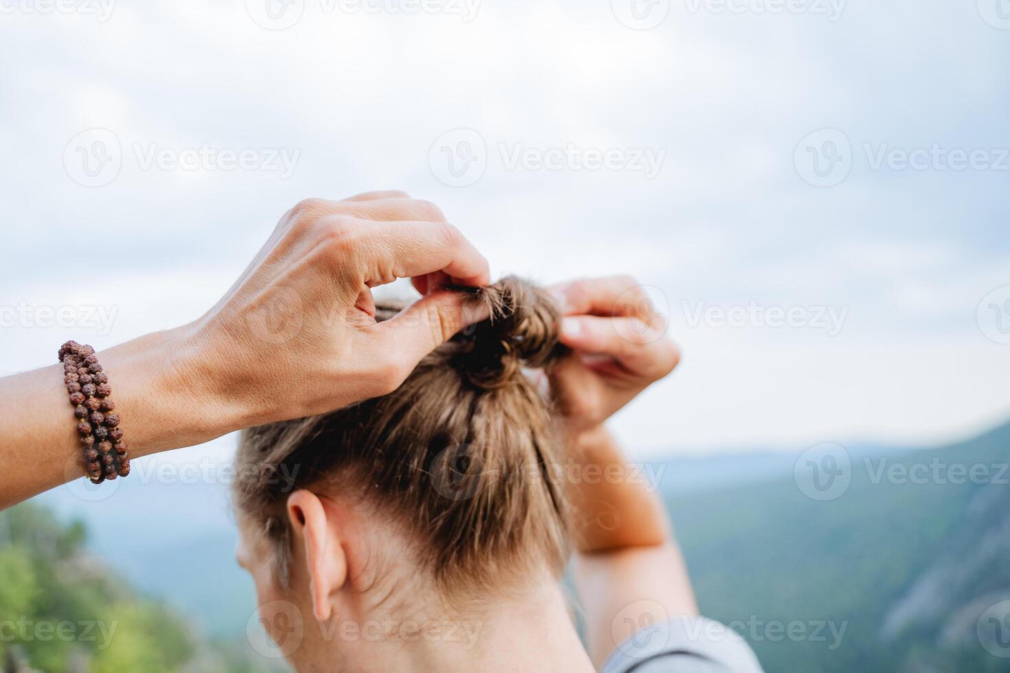 The guy collects his hair in a bun with his hands, the man ties a pigtail on his head, long male hair from behind, the back of the head, make a knot with his hands. photo
