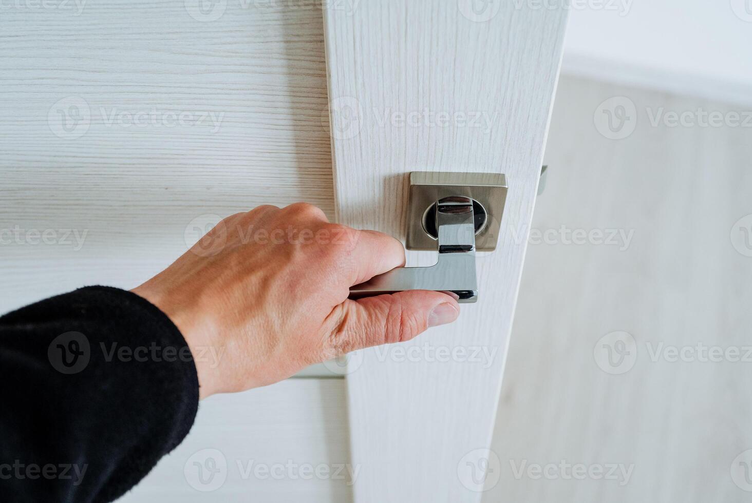The man's hand opens the door to the room, the man holds on to the door handle, the steel chrome handle, the interior design, enter the house. photo