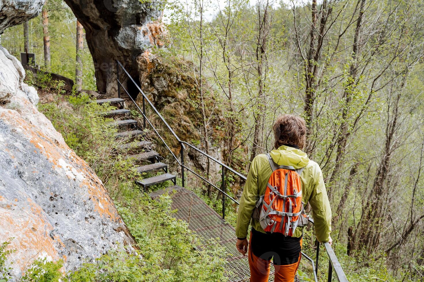 A tourist on a hike with a backpack walks along the trail, a view from behind a person on the way in nature, the national park of the eco-trail, an orange bag for things, equipment for a hike photo