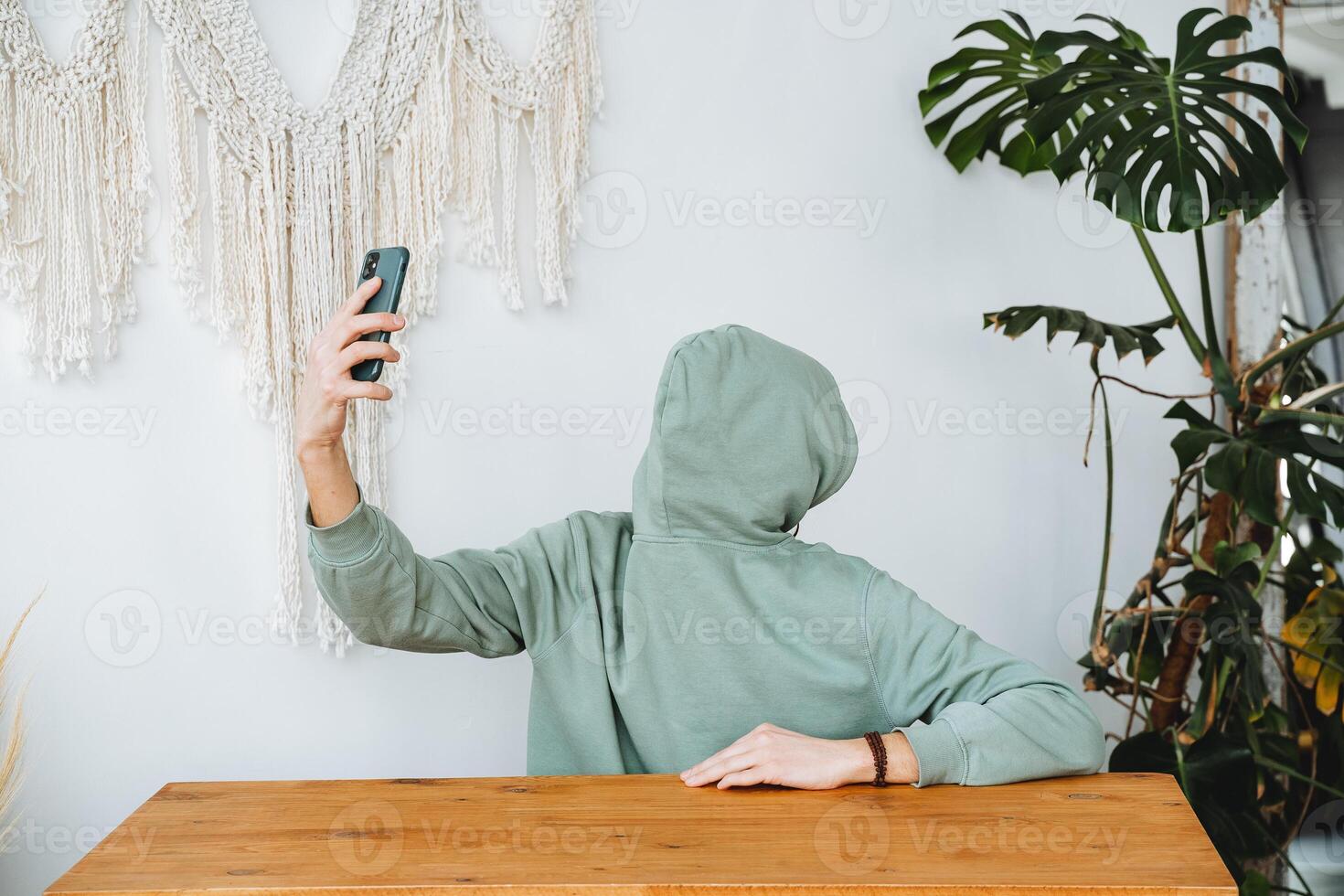 A man without a face takes a selfie of himself. Unrecognizable identity, hacker hiding from the camera, a green sweatshirt, a phone in his hand to hold. photo