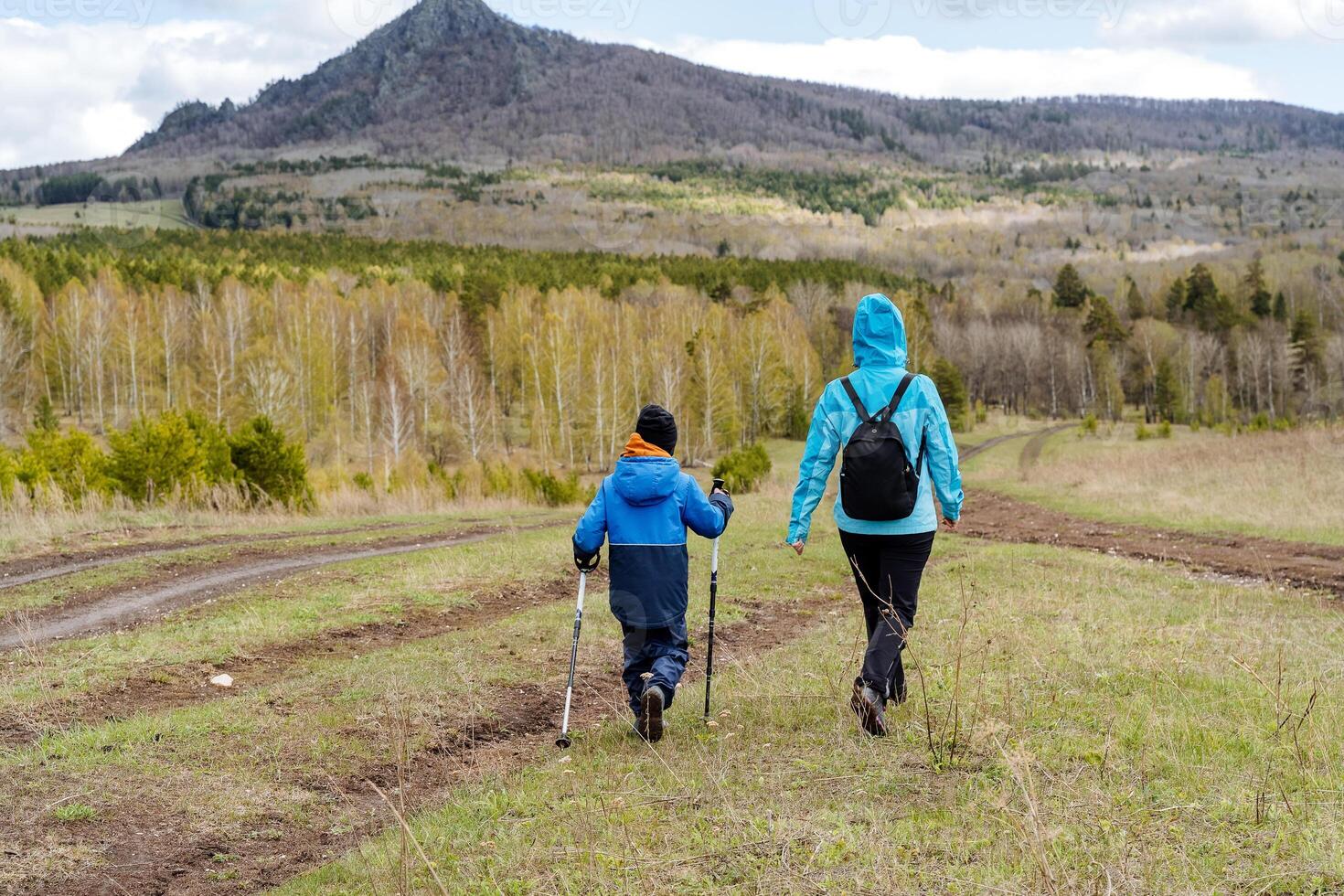 Spring hike to the mountain with a child, a family trip, mother and son walk along the road in the forest, trekking in the mountains, a walk with children in the fresh air. photo