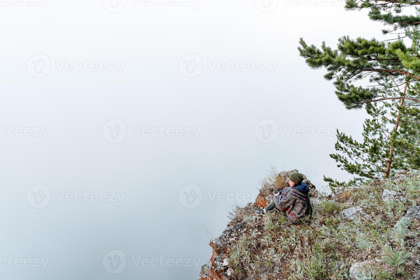a young girl of European appearance dressed in a poncho meditates in nature, sitting in the Lotus position on the edge of a cliff in the early morning, Zen photo