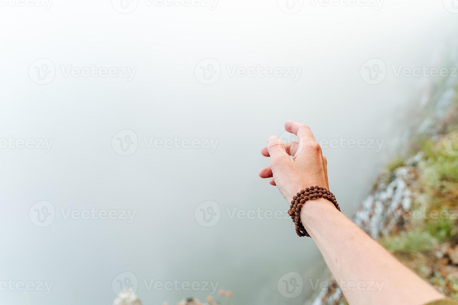 hand with a Rudraksha bracelet on the background of fog, fog in the mountains, morning photo