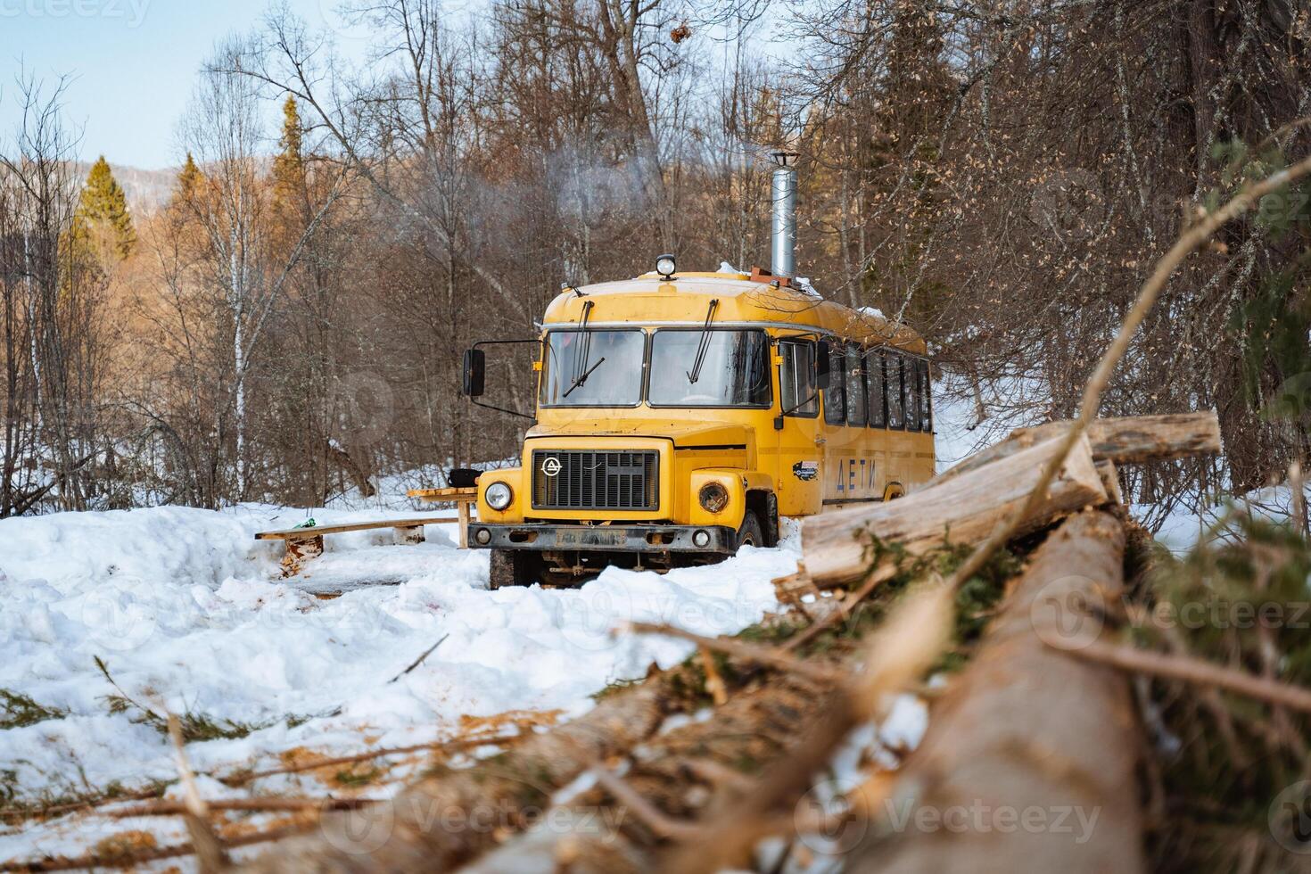 The yellow bus is parked in the winter forest. The bus was converted into a hut. The bus got stuck in the snow. photo